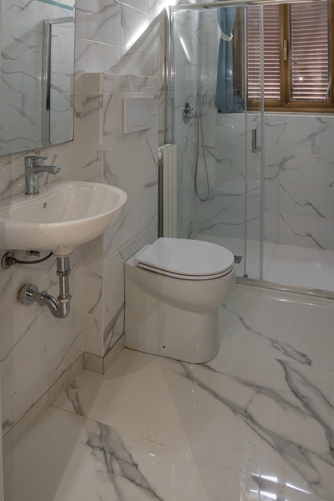 Bagno di hotel ristrutturato con lavabo sospeso, wc e box doccia in gres effetto marmo