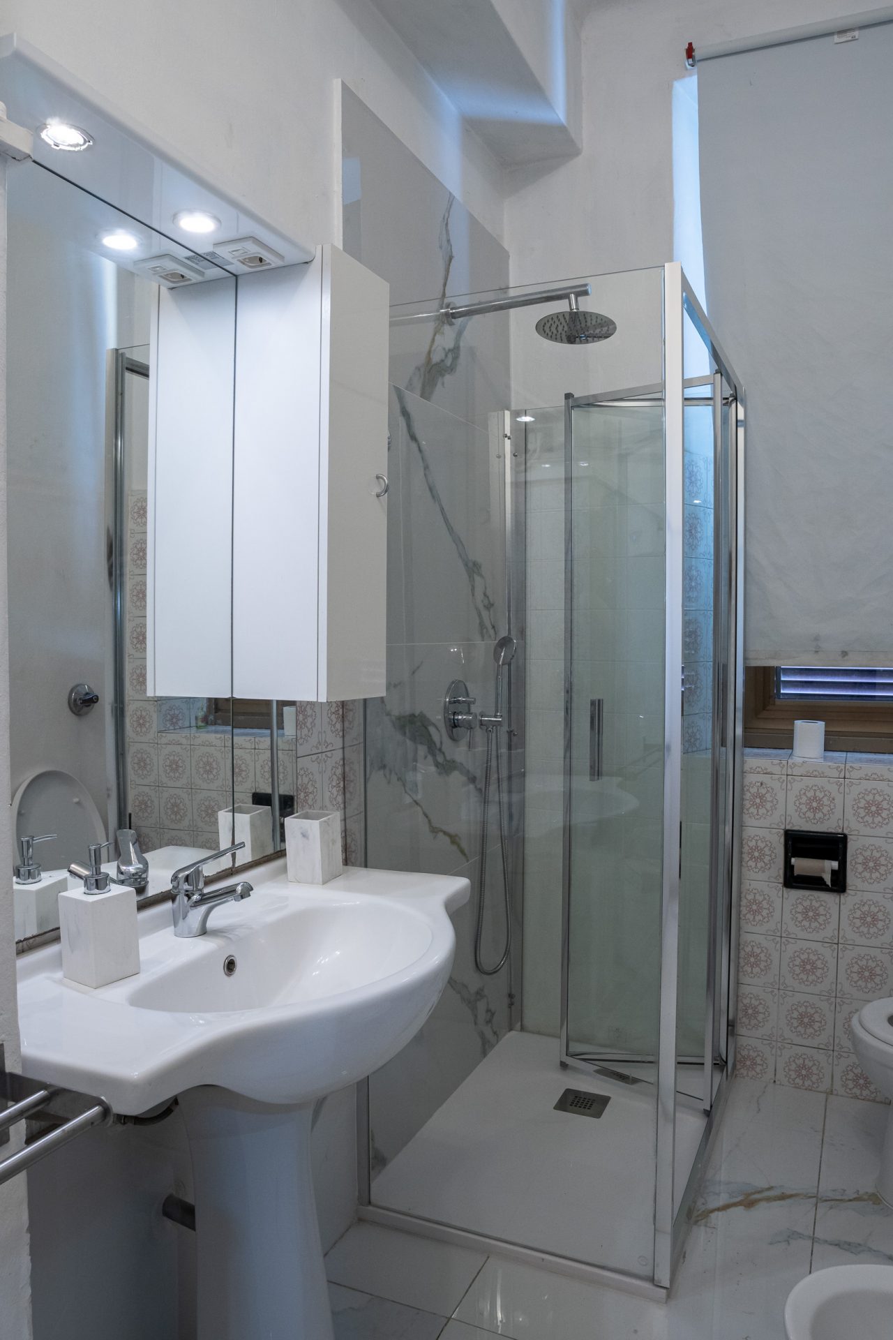 Lavabo a colonna con specchio contenitore illuminato e doccia angolare sul fondo