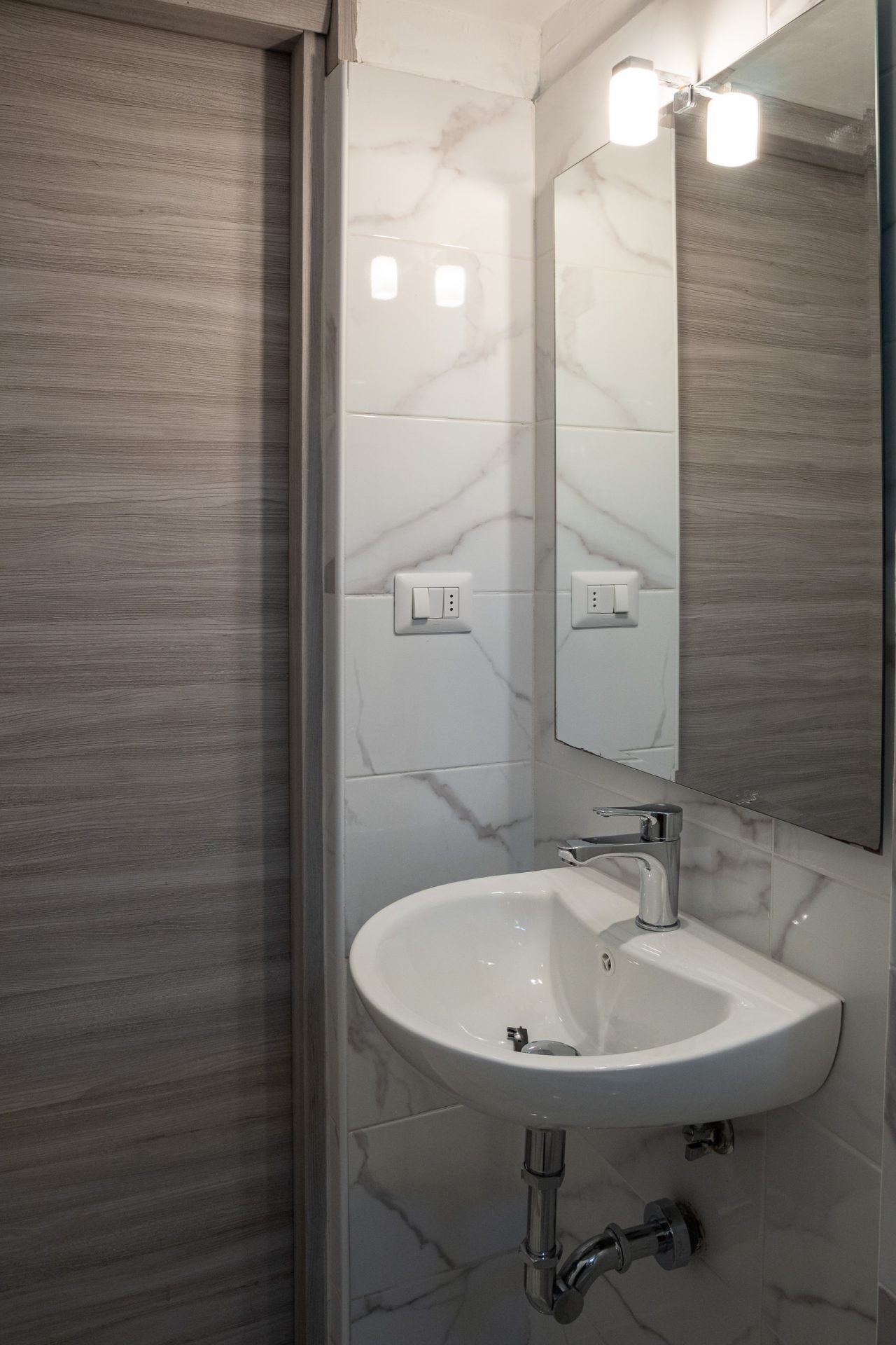 Lavabo sospeso con specchio e applique a due luci nel bagno di camera
