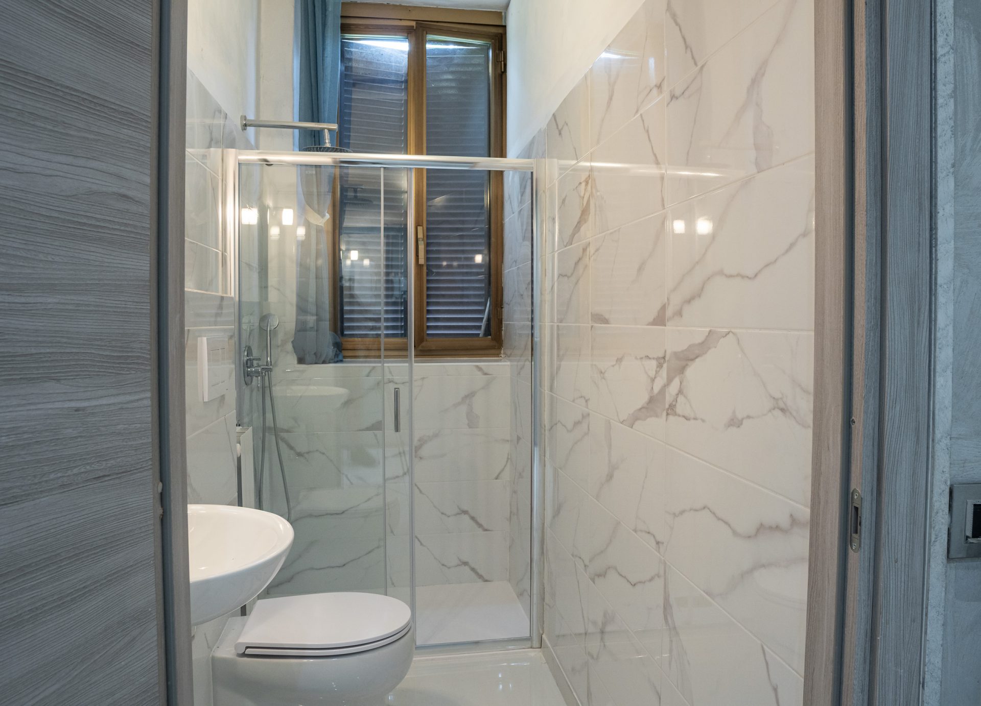 Bagno ristrutturato con parete in gres effetto Calacatta e doccia in cristallo