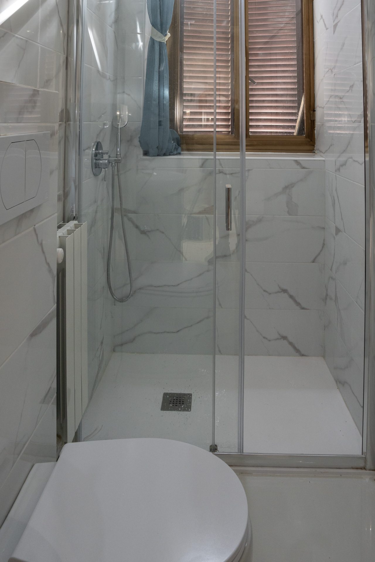 Doccia con porta scorrevole in cristallo e piletta a pavimento nel bagno della camera