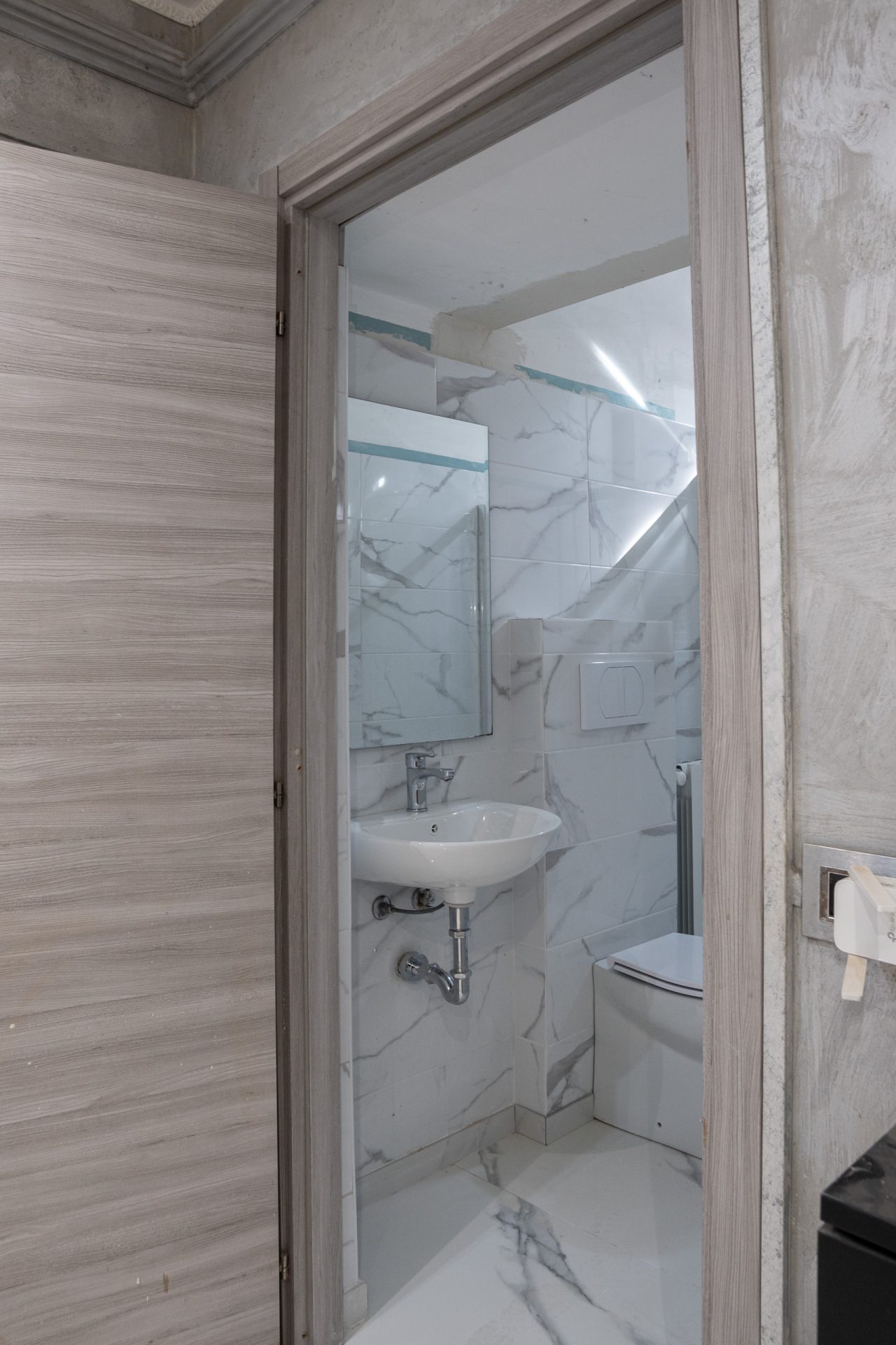Ingresso del bagno di camera visto dalla porta, con lavabo sospeso e specchio